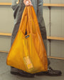 Person holding a yellow reusable bag with a visible brand logo.