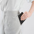 Person wearing light gray pants with a white shirt, holding a black wallet.