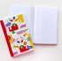 A decorated hardcover notebook with a colorful illustrated cover lies next to an open lined notebook on a plain white background.