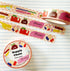 A roll of washi tape featuring a colorful school supply theme, displayed on a lined notebook background alongside a second roll and a small circular product label.