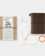 Brown travel notebook with packaging and accessories on a white background
