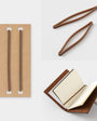 Brown leather notebook with open pages, cardboard holder, and wooden tongs on a white background