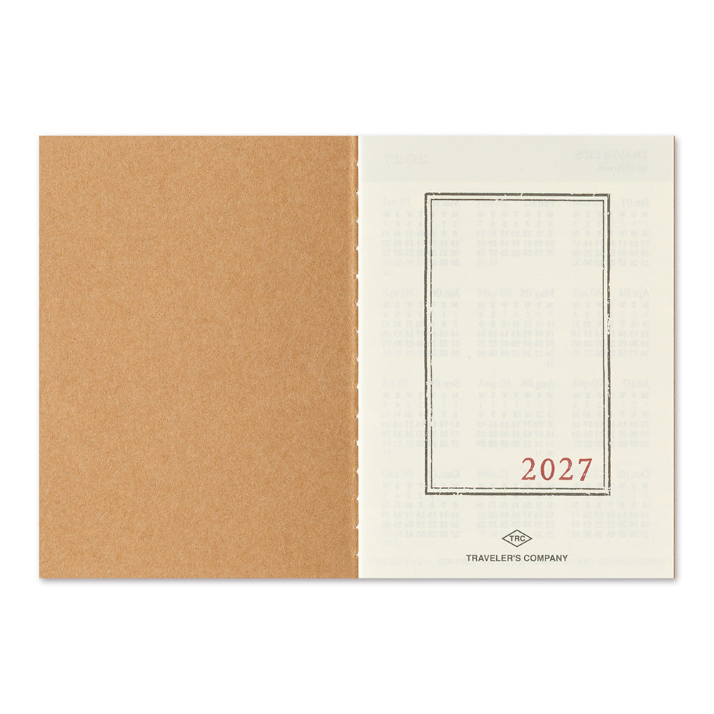An open travel planner or notebook showing a kraft brown textured cover on the left and an off-white interior page on the right with a thin rectangular border, the red text '2027', and small 'Traveler's Company' branding at the bottom.