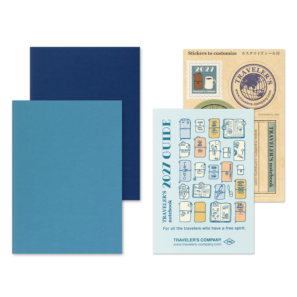 Traveler's Company 2021 guide notebook and sticker set on a white background, featuring a light blue guidebook, a navy blue sheet, a teal blue sheet, and a beige sticker sheet with travel-themed stickers.