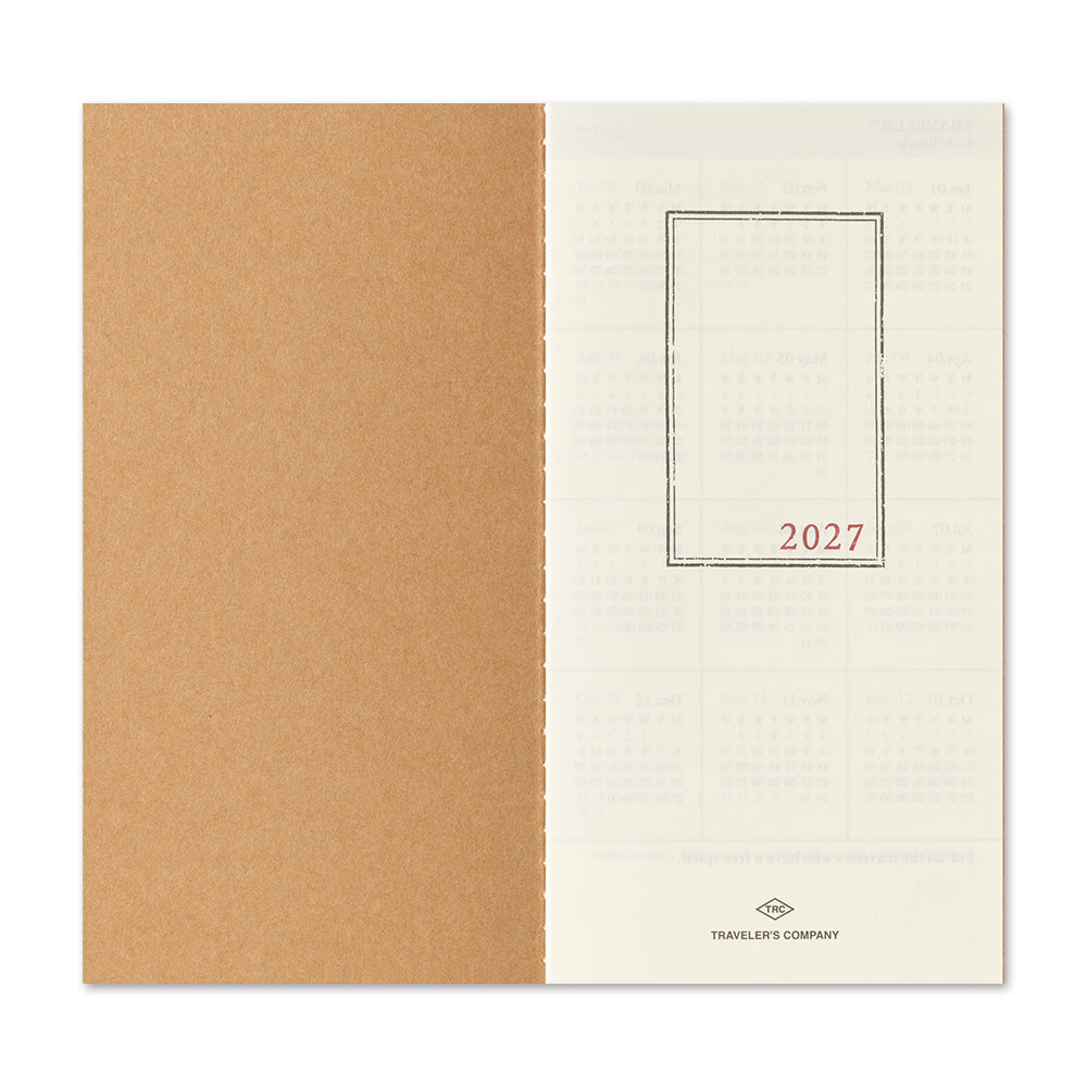 A planner or notebook shown open to a blank page spread, with a large tan kraft-paper left panel and an off-white right panel containing faint calendar grids and the red text '2027' inside a thin rectangular border. Small printed branding at the bottom reads Travelers' Company.