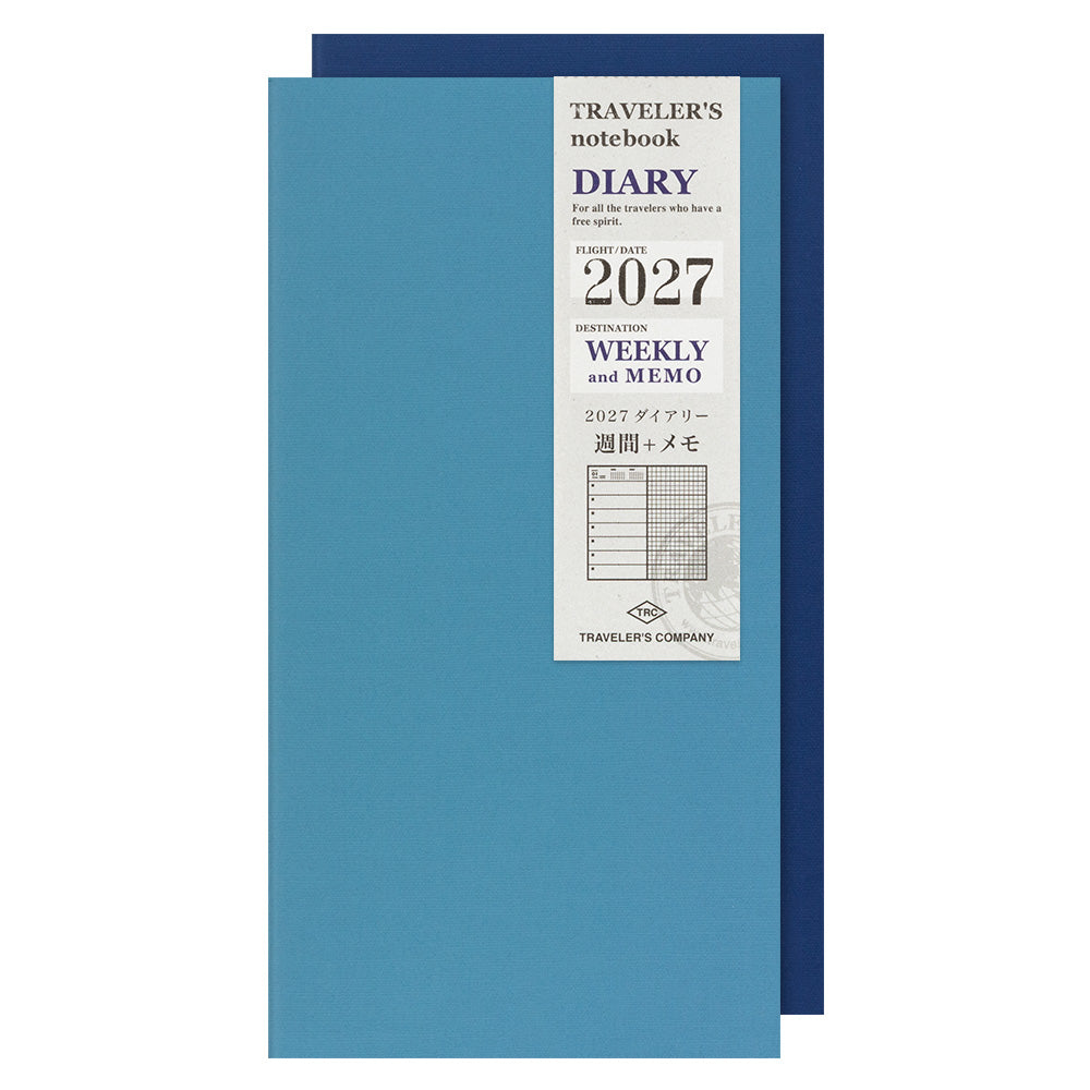 A blue traveler's notebook with a white label on the front, showing '2027' and 'Weekly and Memo' details, with a darker blue notebook partially visible behind it on a white background.