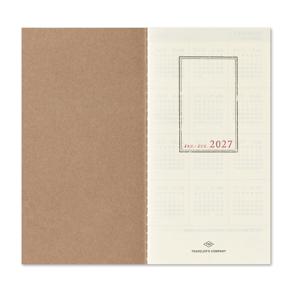 An open planner or notebook showing a kraft brown left page and an off-white right page with faint monthly grids and the red text 'JAN - FEB 2027' plus 'Traveler's Company' at the bottom.
