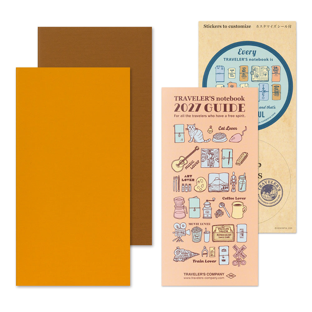 Traveler's notebook set with a bright orange cover, a brown notebook partially visible behind it, and a peach-colored sticker sheet labeled 'Traveler's notebook 2027 Guide' showing illustrated travel-themed stickers.