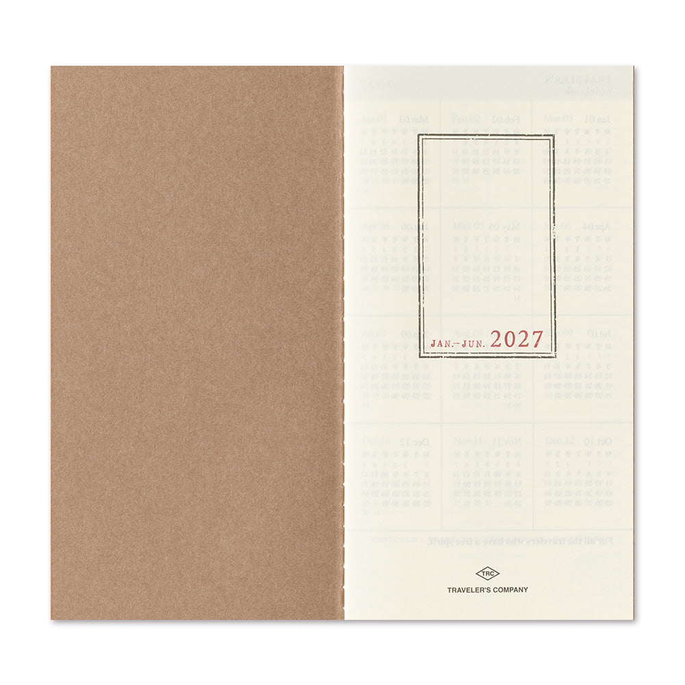An open planner or calendar showing a kraft brown left page and an off-white right page with faint monthly grids and the red text 'JAN - FEB 2027' inside a thin rectangular border. The brand name 'Traveler's Company' appears at the bottom of the right page.