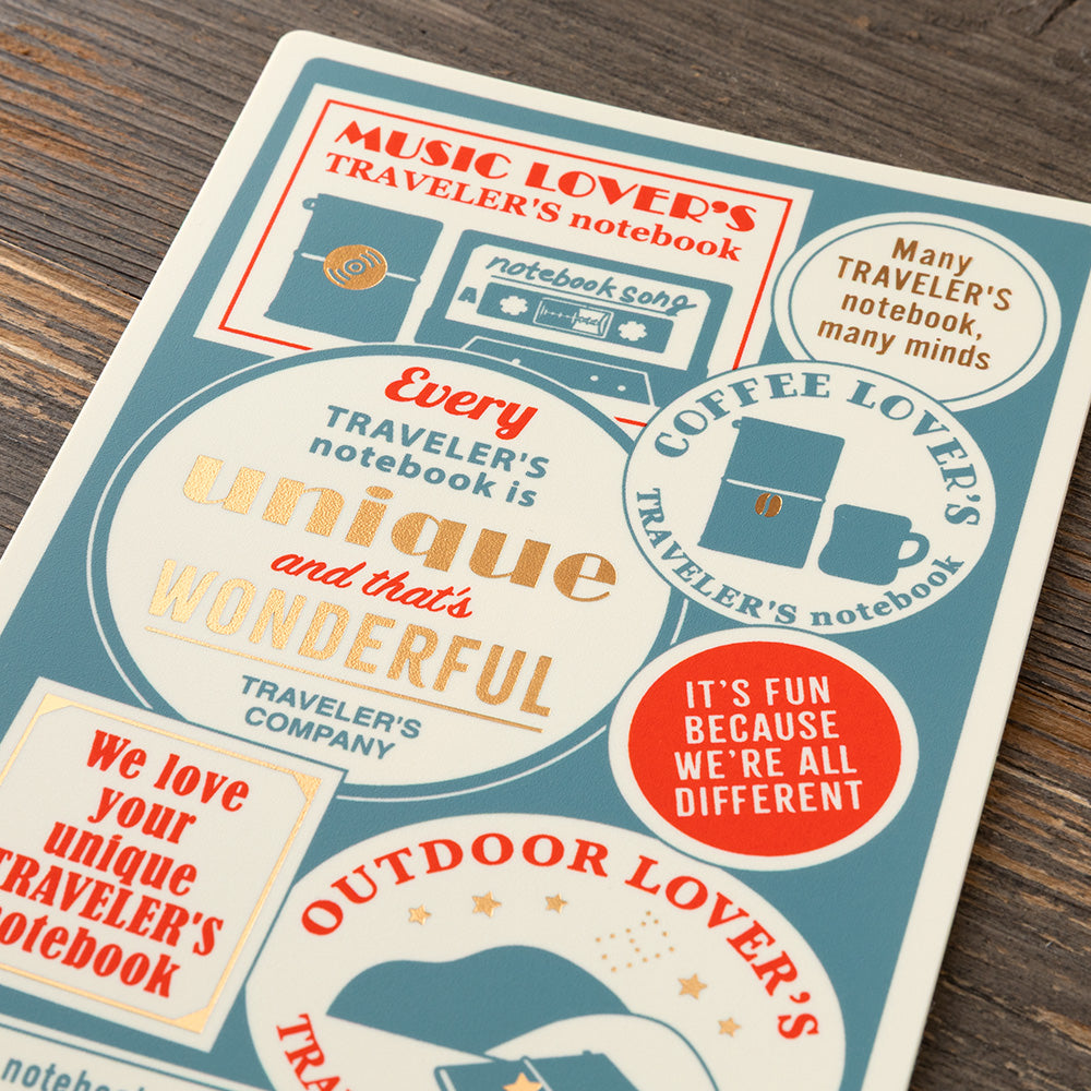A rectangular notebook or book cover laid on a dark wood surface, featuring retro-style illustrated labels and phrases such as 'Music Lover's Traveler's Notebook' and 'Every traveler's notebook is unique and that is wonderful.' The product fills most of the frame at an angle, with visible printed graphics and no person or animal present.