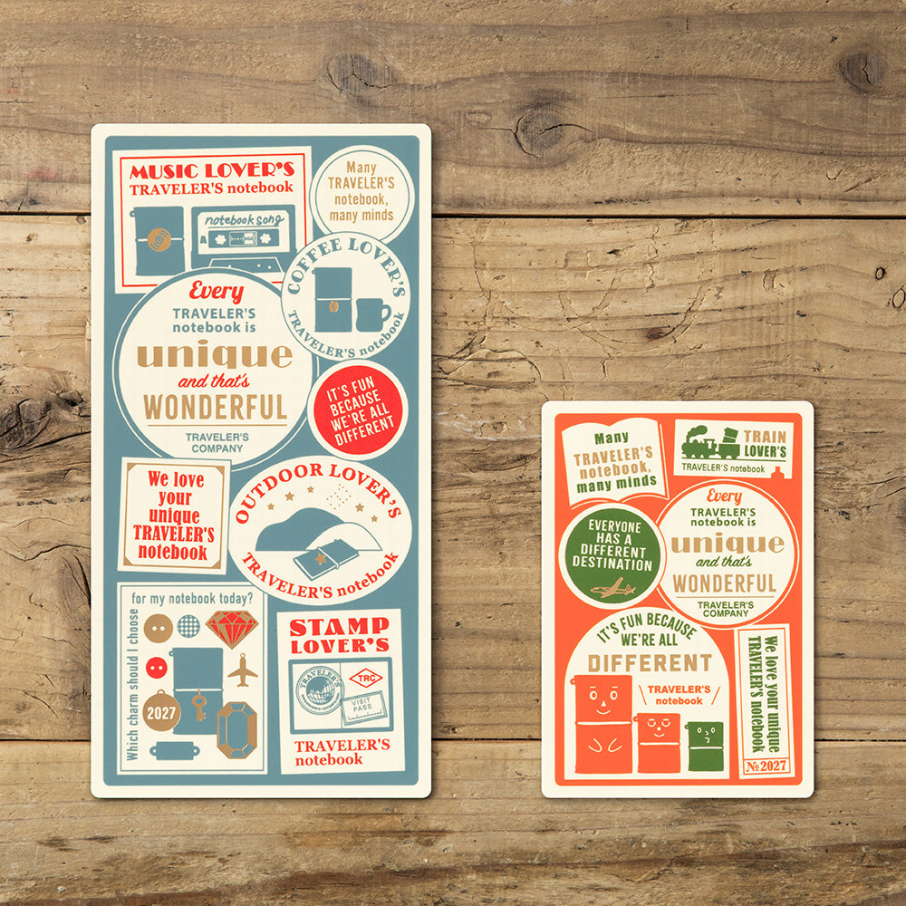 Two rectangular printed cards or stickers with vintage travel-themed typography and small illustrations, displayed on a rustic wooden surface. One card is cream with blue and red text/graphics, and the other is coral red with blue and cream text/graphics.