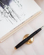Black fountain pen with gold accents on a white surface next to a book with sketches.