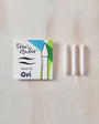 Tom's Studio Ori brush tip packaging with three white candles on a wooden surface