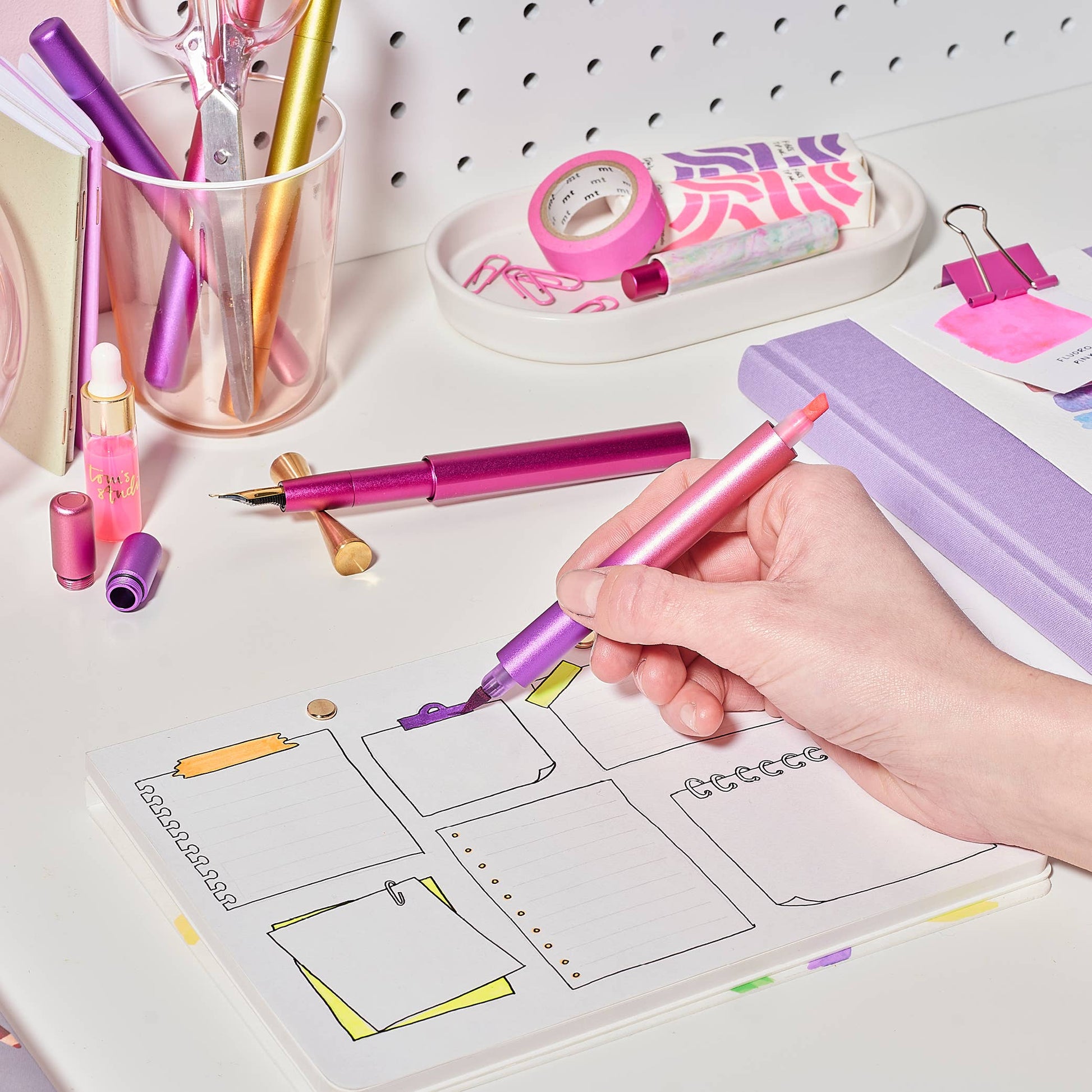 Person using a pink pen on a planner with stationery items in the background