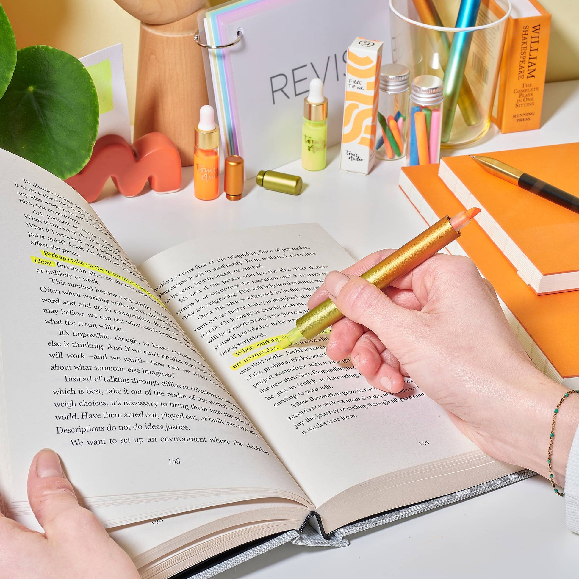 Person using a gold highlighter on an open book with a desk in the background