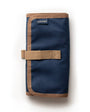 A partially unrolled tool roll with a brown waxed canvas exterior, aluminum hook fastener, and multiple pockets containing pens and other tools.