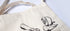Canvas tote bag with black illustrations of stationery items on a white background