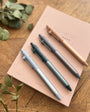 Set of pens on a notebook with greenery on a wooden surface