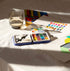 Art supplies including watercolor paints, a glass of water, and a color chart on a white surface.