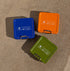 Three portable trash bins in blue, orange, and green on a concrete surface.