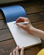 Person writing in a notebook on a wooden surface