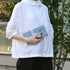 Person wearing a white shirt holding a gray clutch bag outdoors.