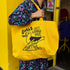Person holding a yellow tote bag with a graphic design and text.