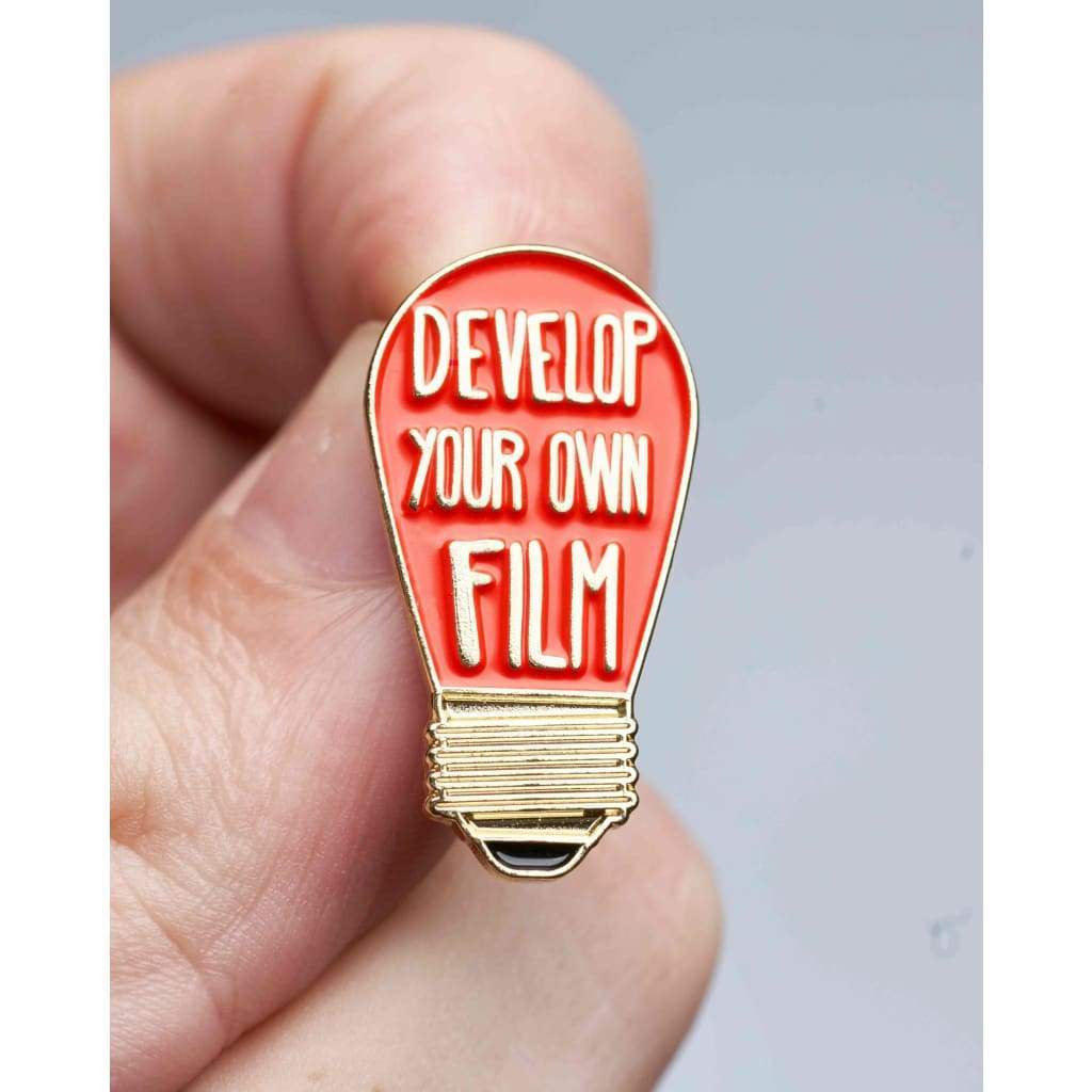 Light bulb-shaped pin with 'Develop Your Own Film' text held between fingers