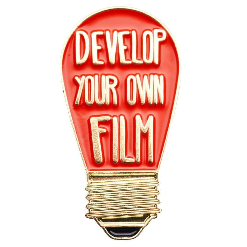 A light bulb-shaped enamel pin with a red body, gold metal outline and screw base, and raised cream lettering that reads 'DEVELOP YOUR OWN FILM' on a plain white background.