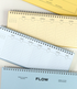 Three spiral-bound weekly planner notebooks in pastel blue, cream, and yellow, arranged diagonally on a white surface. The bottom notebook features the brand name 'FLOW' printed prominently on its cover.