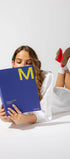 Woman reading a blue book with a yellow 'M' on a white background