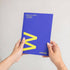 Person holding a blue planner with a yellow 'M' on a white background